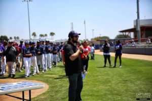 Dr. Jason von Stietz stands in a baseball field holding a microphone speaking at the Urban Youth Academy