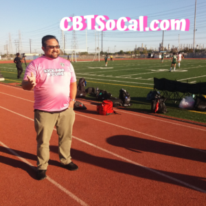 Dr. Jason von Stietz wears a shirt that says "Kick for a Cure" and stands near a soccer field providing sport psychology services